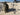WOBIG Portable Tactical Gearstand with a sleek black finish, featuring a central pole and a horizontal crossbar, set up on a grassy lawn with a backdrop of sand and dirt